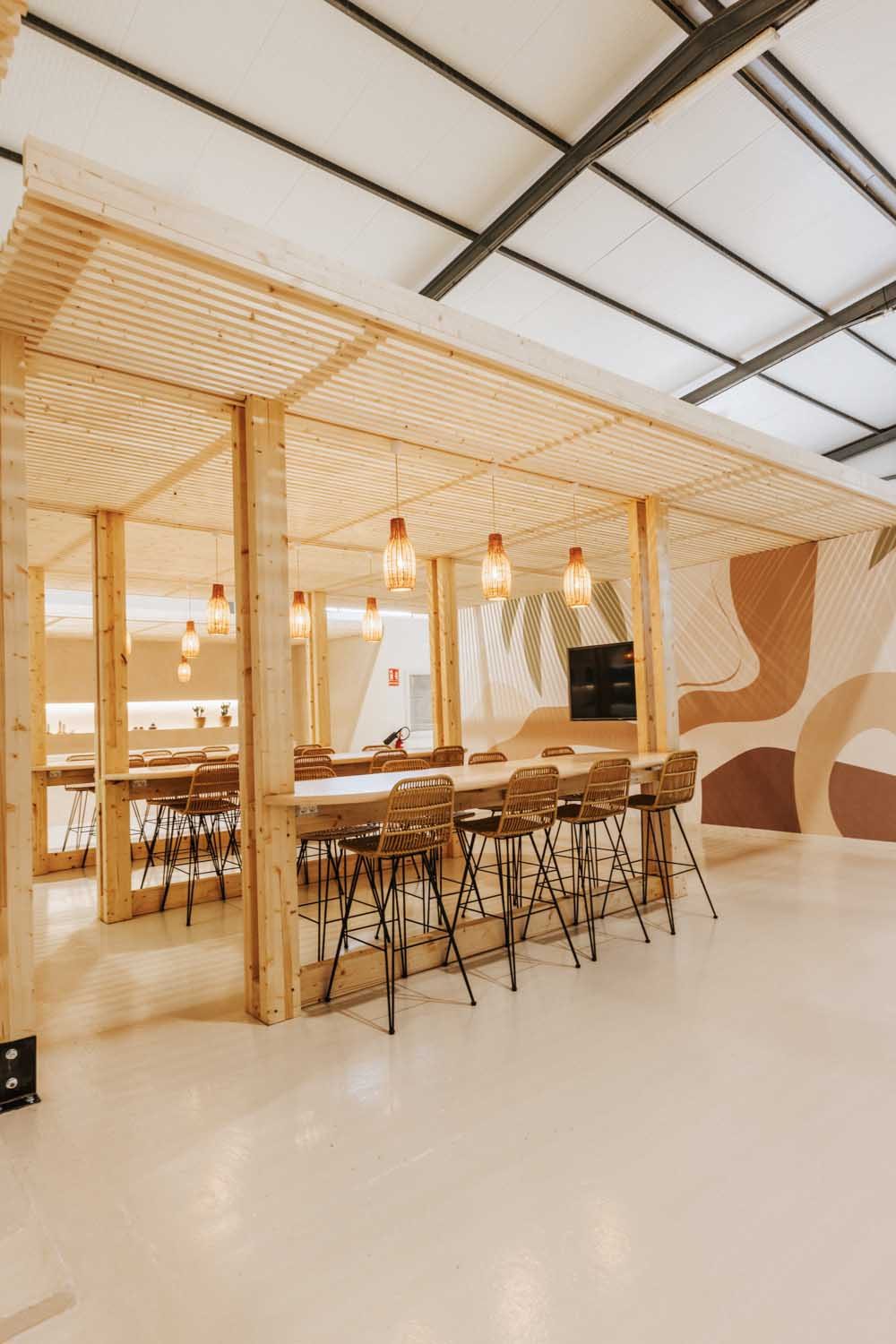 Long dining table beneath the pergola with pendant lights and a wall mural