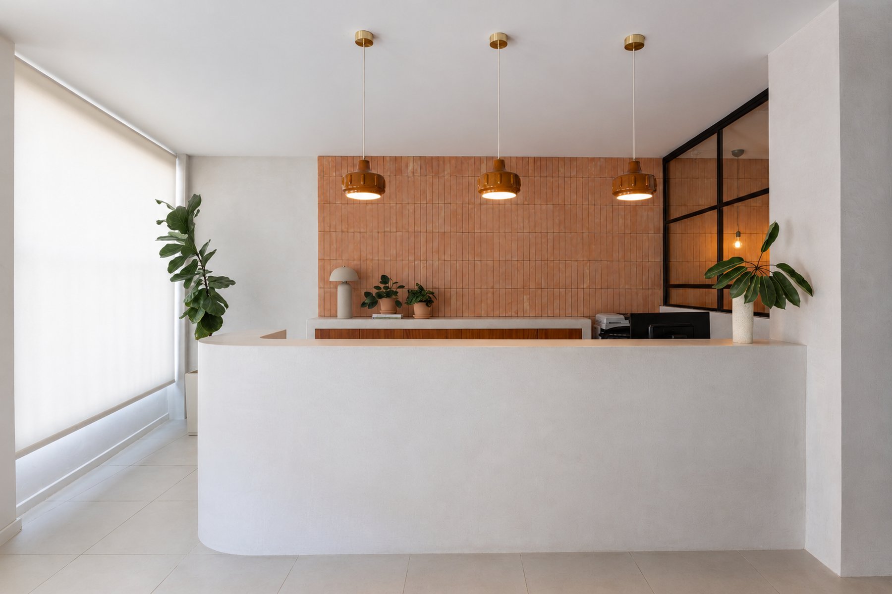 Wide view of the curved reception desk beneath three brass pendant lights, glass-partitioned office beyond