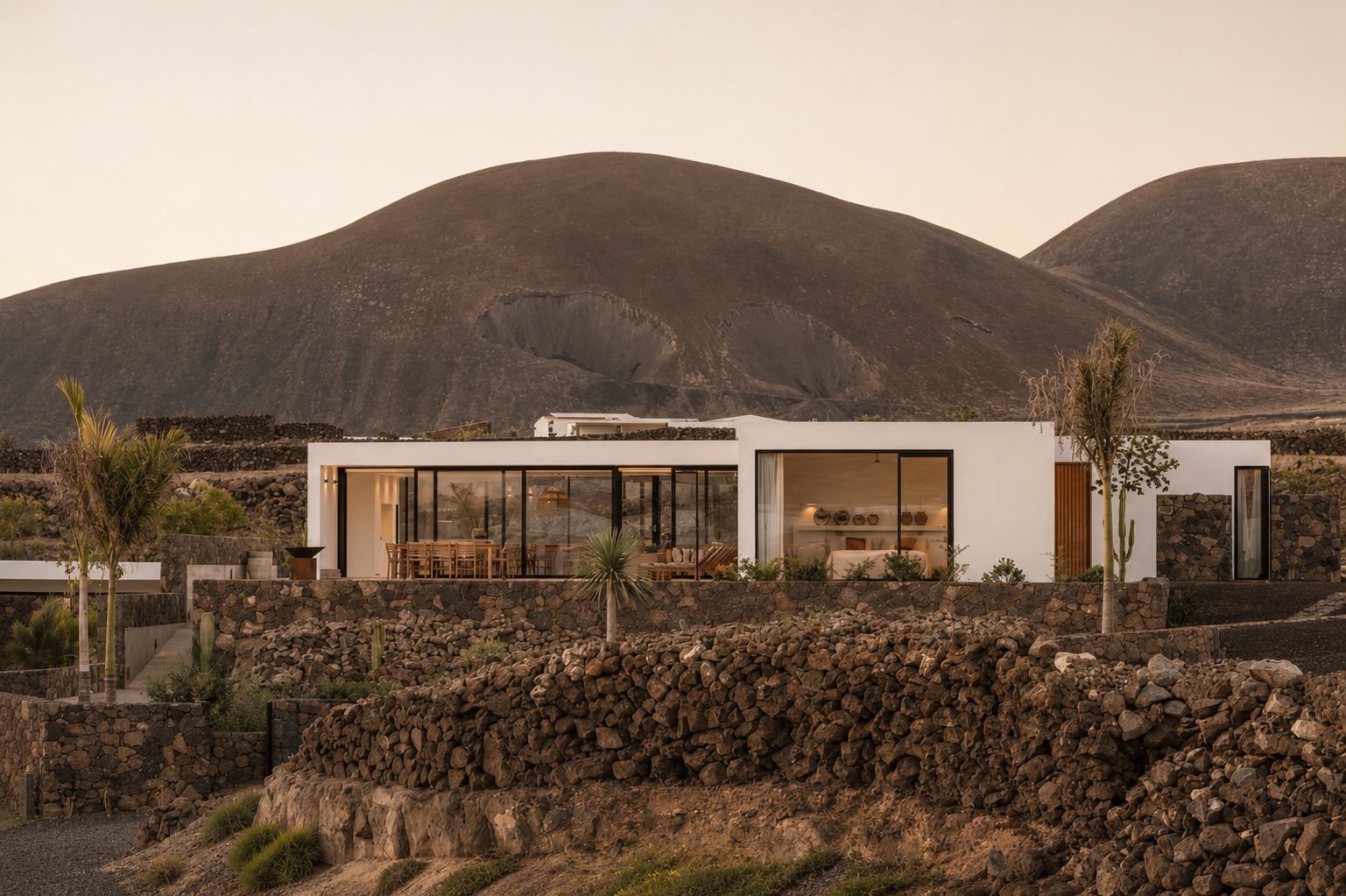 Modern white villa nestled among volcanic hills, framed by a dry-stone boundary wall